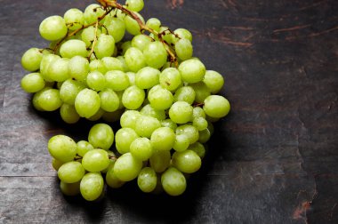Olgun yeşil üzümlü ve su damlalı bir dal. Tahta arka planda sulu üzümler, yakın plan. Fotokopi alanı olan koyu mutfak masasında üzümler
