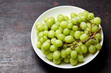 Tabakta su damlaları olan olgun yeşil üzüm dalı. Tahta arka planda sulu üzümler, yakın plan. Fotokopi alanı olan koyu mutfak masasında üzümler