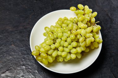 Tabakta olgun üzüm dalı var. Tahta arka planda sulu üzümler, yakın plan. Fotokopi alanı olan koyu mutfak masasında üzümler