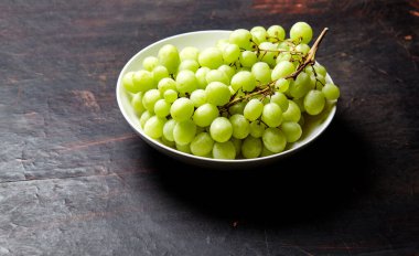 Tabakta olgun yeşil üzüm dalı var. Tahta arka planda sulu üzümler, yakın plan. Fotokopi alanı olan koyu mutfak masasında üzümler