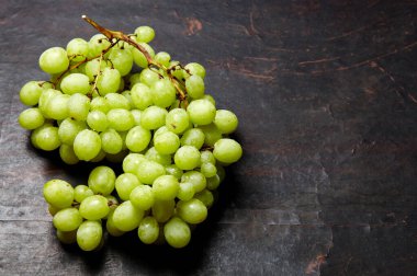 Olgun yeşil üzümlü ve su damlalı bir dal. Tahta arka planda sulu üzümler, yakın plan. Fotokopi alanı olan koyu mutfak masasında üzümler