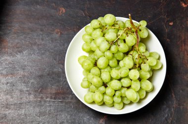 Tabakta su damlaları olan olgun yeşil üzüm dalı. Tahta arka planda sulu üzümler, yakın plan. Fotokopi alanı olan koyu mutfak masasında üzümler
