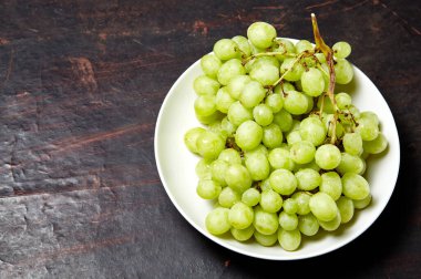 Tabakta su damlaları olan olgun yeşil üzüm dalı. Tahta arka planda sulu üzümler, yakın plan. Fotokopi alanı olan koyu mutfak masasında üzümler