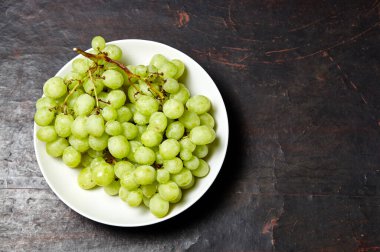Tabakta su damlaları olan olgun yeşil üzüm dalı. Tahta arka planda sulu üzümler, yakın plan. Fotokopi alanı olan koyu mutfak masasında üzümler