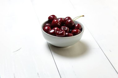 Ahşap arka planda seramik bir kasede tatlı kirazlar, yakın plan. Taze taze kirazlar bir kase içinde su damlacıkları