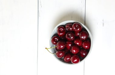 Ahşap arka planda seramik bir kasede tatlı kirazlar, yakın plan. Bir kase dolusu su damlacıkları olan taze kirazlar.