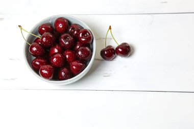 Ahşap arka planda seramik bir kasede tatlı kirazlar, yakın plan. Bir kase dolusu su damlacıkları olan taze kirazlar.