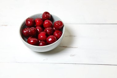 Ahşap arka planda seramik bir kasede tatlı kirazlar, yakın plan. Taze taze kirazlar bir kase içinde su damlacıkları