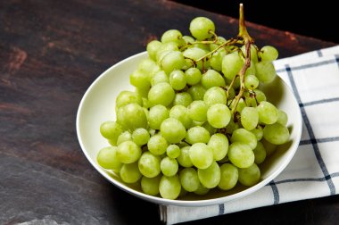 Tabakta su damlaları olan olgun yeşil üzüm dalı. Tahta arka planda sulu üzümler, yakın plan. Fotokopi alanı olan koyu mutfak masasında üzümler