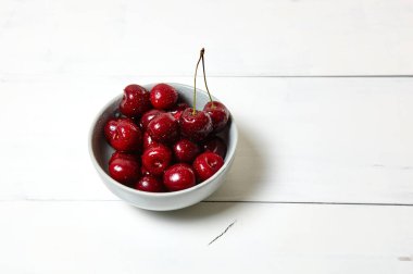 Ahşap arka planda seramik bir kasede tatlı kirazlar, yakın plan. Taze taze kirazlar bir kase içinde su damlacıkları