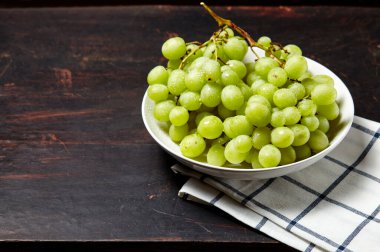 Tabakta su damlaları olan olgun yeşil üzüm dalı. Tahta arka planda sulu üzümler, yakın plan. Fotokopi alanı olan koyu mutfak masasında üzümler