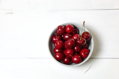 Ahşap arka planda seramik bir kasede tatlı kirazlar, yakın plan. Bir kase dolusu su damlacıkları olan taze kirazlar.