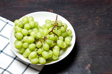 Tabakta su damlaları olan olgun yeşil üzüm dalı. Tahta arka planda sulu üzümler, yakın plan. Fotokopi alanı olan koyu mutfak masasında üzümler