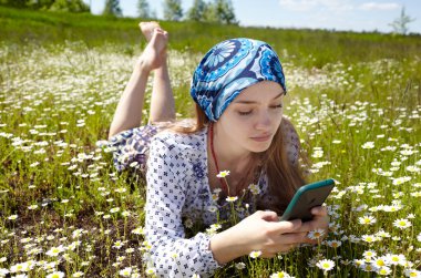 Çekici genç bir kadın bahar otlağında akıllı telefonunda daktilo çekiyor. Mutlu hipster kızın portre fotoğrafı. Doğada rahatlıyor ve iyi vakit geçiriyor.
