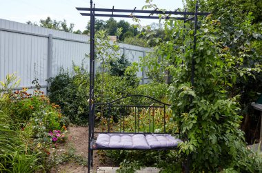 Çiçekler ve süslü çalılarla çevrili metal bankların olduğu bahçe dinlenme yeri. Arka bahçede dinlenecek bir yer. Hafta sonu için rahat bir yer. Bahçede rahatla.