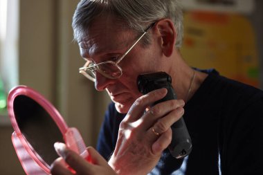 Elektrikli jileti olan son sınıf öğrencisi. Sakalını kesen küçük aynalı bir adam. Seçici odak, bulanık arkaplan, sığ dof