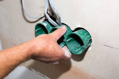 İnsanlar elektrik üretiyor. Bakım onarımı dairede tadilat yapıyor. Kapalı alanda restorasyon. Duvardaki deliklerde soket anahtarları için renkli kablolar var..