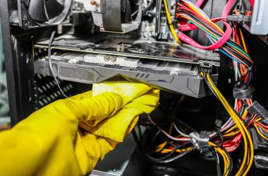 Inside details of the personal computer. Man is cleaning wires in yellow gloves. Motherboard and video card in the dust. Broken PC.