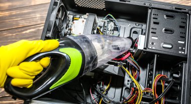 Inside details of the personal computer. Man is cleaning wires with vacuum cleaner. Small hoover. Motherboard and video card in the dust. Broken PC.