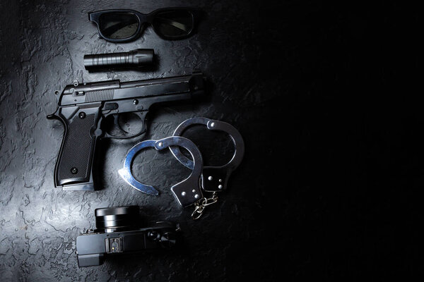 Black gun, flashlight, glasses, camera and Police metal real handcuffs lie on the black background. Private detective work. Searching information. Crime and robbery, prison concept.