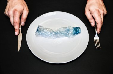 Plastik şişeler tabakta. Kirli yiyecekler yiyen insanlar. Çevresel bir sorun. Ekolojik felaket. Geri dönüşüm sorunu. Bıçak ve çatalla eller.