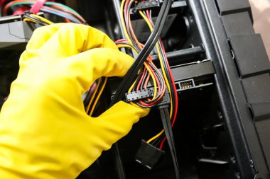 Inside details of the personal computer. Man is cleaning wires in yellow gloves. Motherboard and video card in the dust. Broken PC.