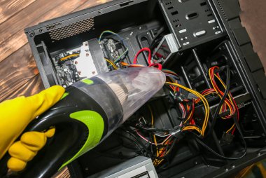 Inside details of the personal computer. Man is cleaning wires with vacuum cleaner. Small hoover. Motherboard and video card in the dust. Broken PC.