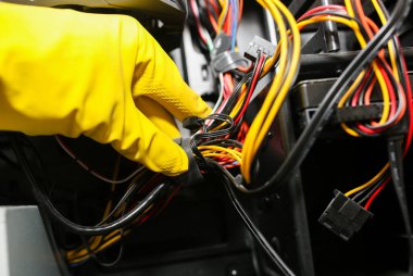 Inside details of the personal computer. Man is cleaning wires in yellow gloves. Motherboard and video card in the dust. Broken PC.