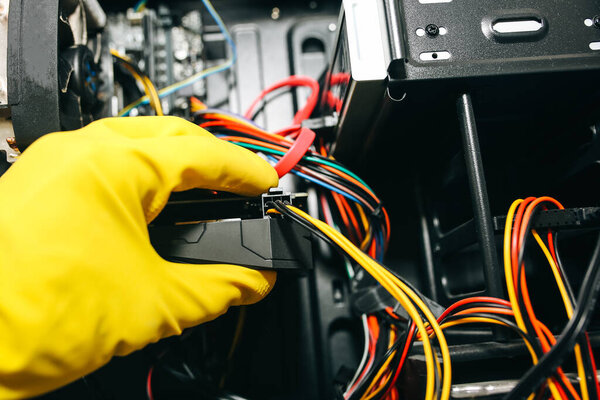 Inside details of the personal computer. Man is cleaning wires in yellow gloves. Motherboard and video card in the dust. Broken PC.