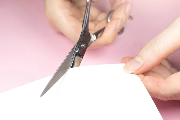 Woman is cutting white paper with scissors, close up.