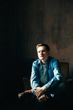 Fotoğraf stüdyosundaki koltukta oturan kot ya da kot elbiseli şık genç adamın portresi..