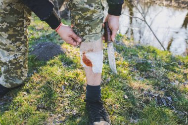 Adam kanayan yaraya bandaj yapıyor. Yaralı bacak. Doğada bir turist. Enfeksiyon tehlikesi. Tıbbi tedavi. Yürüyüş travması.