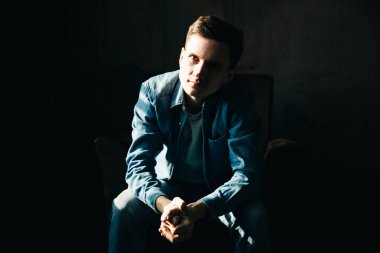 Fotoğraf stüdyosundaki koltukta oturan kot ya da kot elbiseli şık genç adamın portresi..