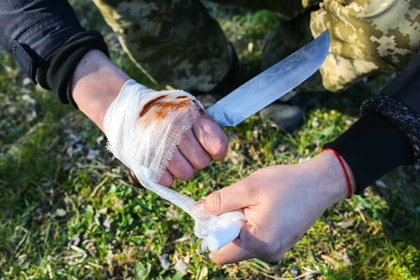 Man is putting bandage on bleeding wound. Injured hand. Cut with a knife. Tourist in the nature. Infection danger. Medical treatment.