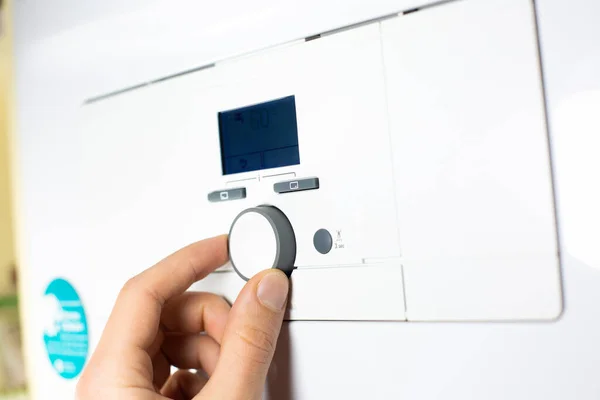 Fingers adjust Gas boiler control panel for hot water and heating. Buttons and a digital display. Concept of home heating and heat conservation.