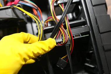 Inside details of the personal computer. Man is cleaning wires in yellow gloves. Motherboard and video card in the dust. Broken PC.