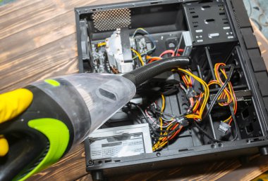 Inside details of the personal computer. Man is cleaning wires with vacuum cleaner. Small hoover. Motherboard and video card in the dust. Broken PC.
