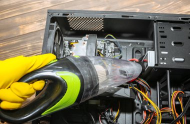 Inside details of the personal computer. Man is cleaning wires with vacuum cleaner. Small hoover. Motherboard and video card in the dust. Broken PC.