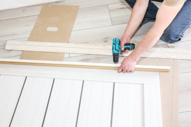 Adam kapıları kuruyor. Marangoz menteşelerde matkapla delikler açıyor. Onarım işe yarıyor. Dairede bakım var..