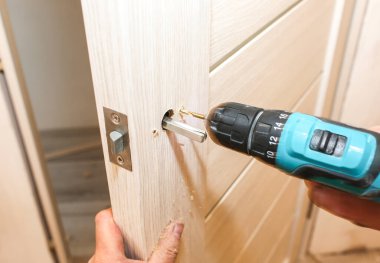 Adam matkapla kapı kolunu kuruyor. Onarım işe yarıyor. Dairede bakım var..