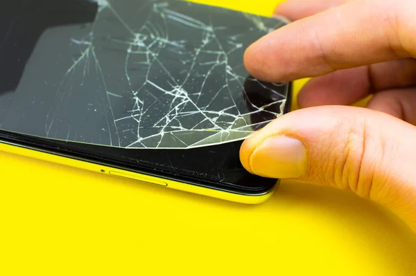Man replacing the broken tempered glass screen protector. Crashed smartphone. Close up.