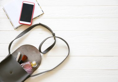 Telefon, şık çanta ve beyaz arka planda parfümler. Güzel düz bir yatak. İş kadını için eşyalar. Not defteri çizelgesi. Makyaj seti.