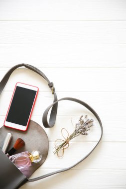 Phone, stylish bag and perfumes on white background. Beautiful flat lay. Things for business woman. Note book schedule. Makeup kit. Lavender bouquet.