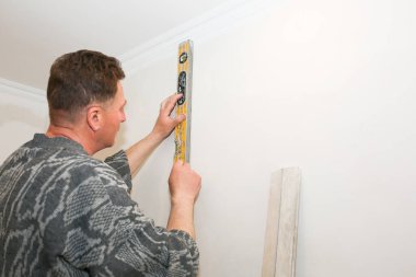 Man is holding a spirit level in hands. Hanging of wallpapers. Maintenance repair works renovation in the flat. Restoration indoors. Work in process.