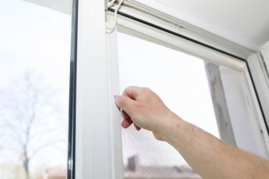 Man is installing the mosquito net on the window. Protection from bugs.
