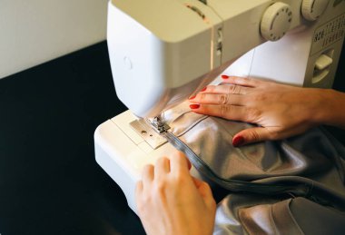 Woman is working at sewing machine. Girls hands with red manicure. Fashion concept. Creating of new clothes process. Hobby ideas.