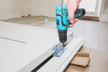 Adam kapıları kuruyor. Marangoz menteşelerde matkapla delikler açıyor. Onarım işe yarıyor. Dairede bakım var..