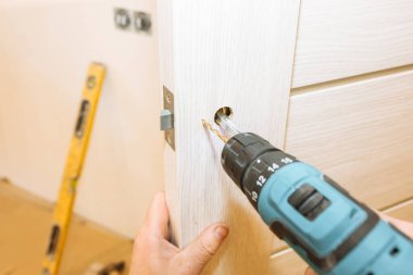 Adam matkapla kapı kolunu kuruyor. Onarım işe yarıyor. Dairede bakım var..