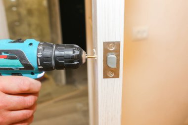 Adam matkapla kapı kolunu kuruyor. Onarım işe yarıyor. Dairede bakım var..