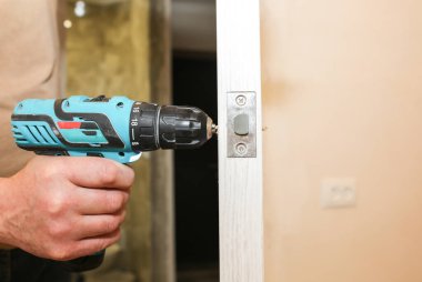 Adam matkapla kapı kolunu kuruyor. Onarım işe yarıyor. Dairede bakım var..